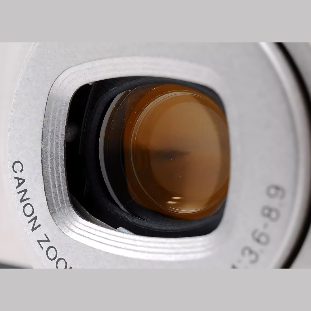 Extreme close-up of Canon Prima Super 135 square lens opening with ribbed silver ring and warm amber coated glass element at ClubCamera.com