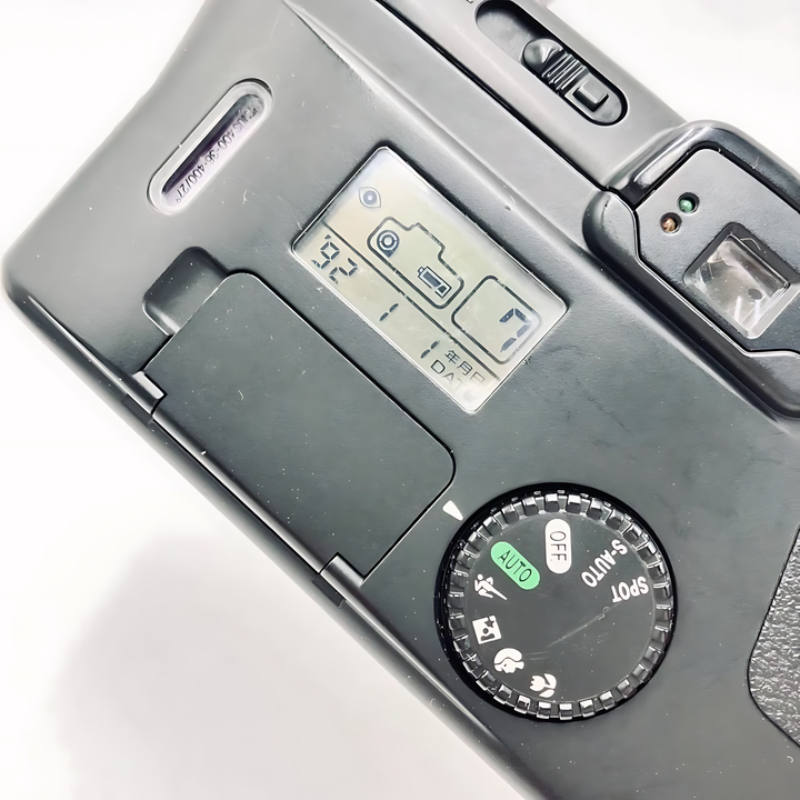 Top rear control panel close-up of Canon Prima Super 135 with tactile mode dial, green AUTO light, and LCD screen showing exposure data from ClubCamera.com