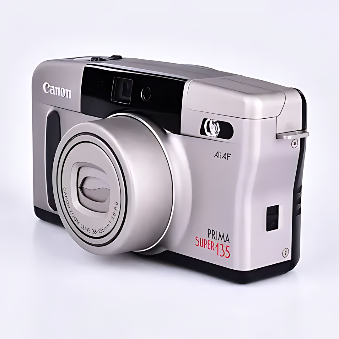Front-three-quarter view of silver Canon Prima Super 135 showcasing zoom lens rings and bold red Prima Super 135 branding at ClubCamera.com
