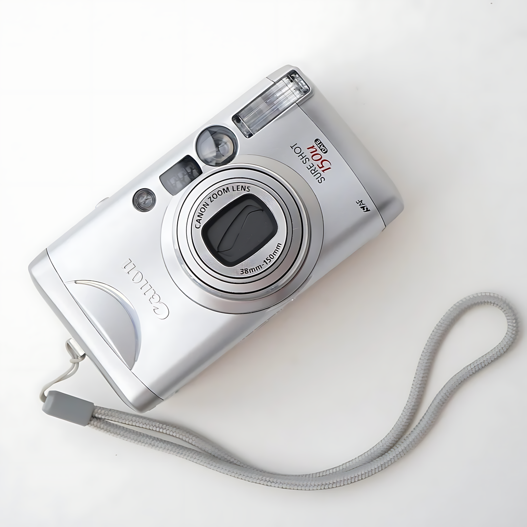 Top down view of silver Canon Sure Shot 150u film camera with lens cap and coiled wrist strap at ClubCamera.com