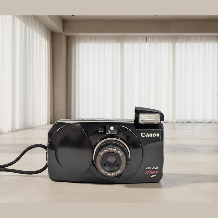 Black Canon Sure Shot 70 Zoom 35mm film camera front view on beige floor with zoom lens ring and wrist strap at ClubCamera.com