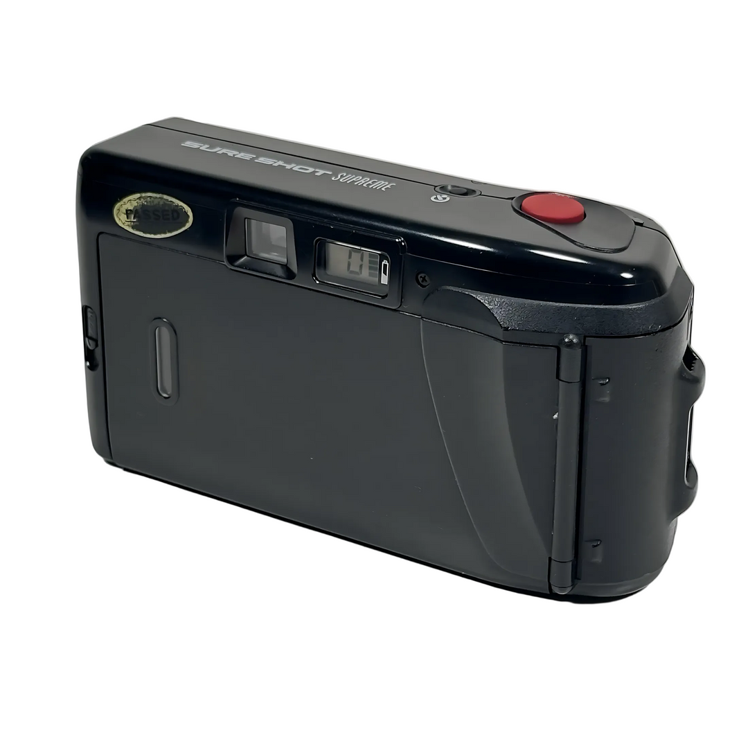 Side profile of black Canon Sure Shot Supreme film camera with silver lettering, red shutter button, LCD counter, and gold tested sticker at ClubCamera.com