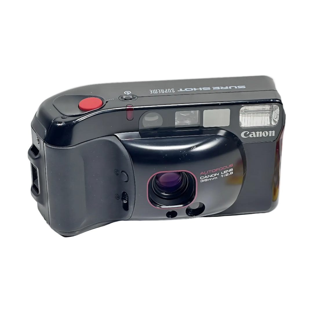 Three-quarter angle of black Canon Sure Shot Supreme film camera showing red shutter button, pink-rimmed lens, and Canon logo at ClubCamera.com