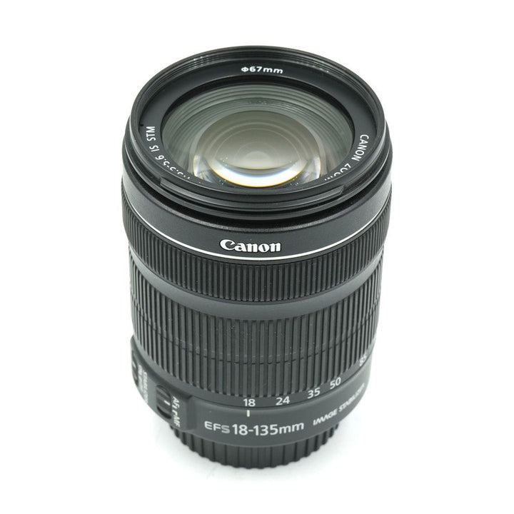 ClubCamera black Canon EF-S 18-135mm side profile showing ribbed grip rings and golden lens coating reflection