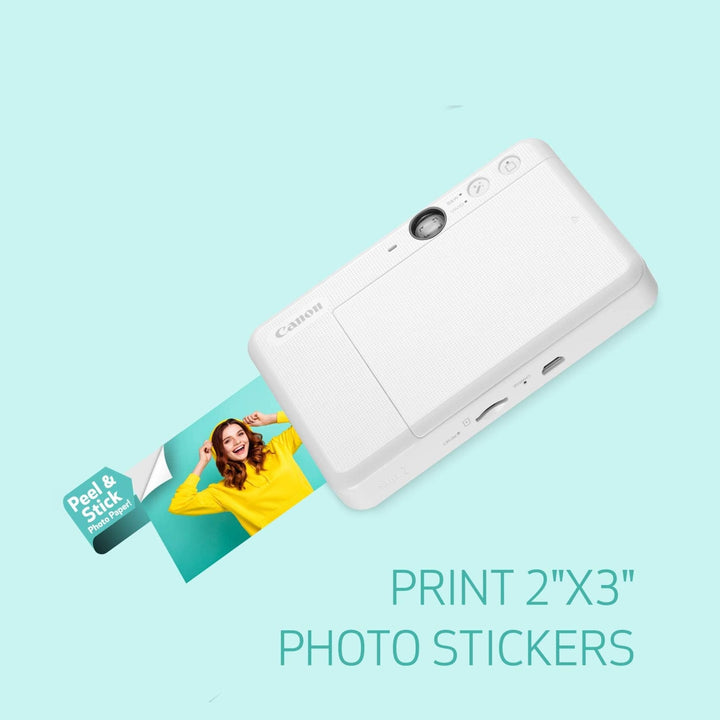 White Canon Ivy Cliq2 printer ejecting 2x3 inch adhesive photo stickers with rear ports visible from ClubCamera.com