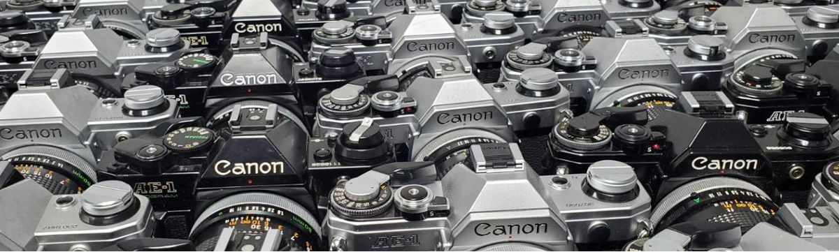A close-up, crowded view of multiple vintage Canon SLR film cameras with silver and black bodies, tightly packed together.ClubCamera.com