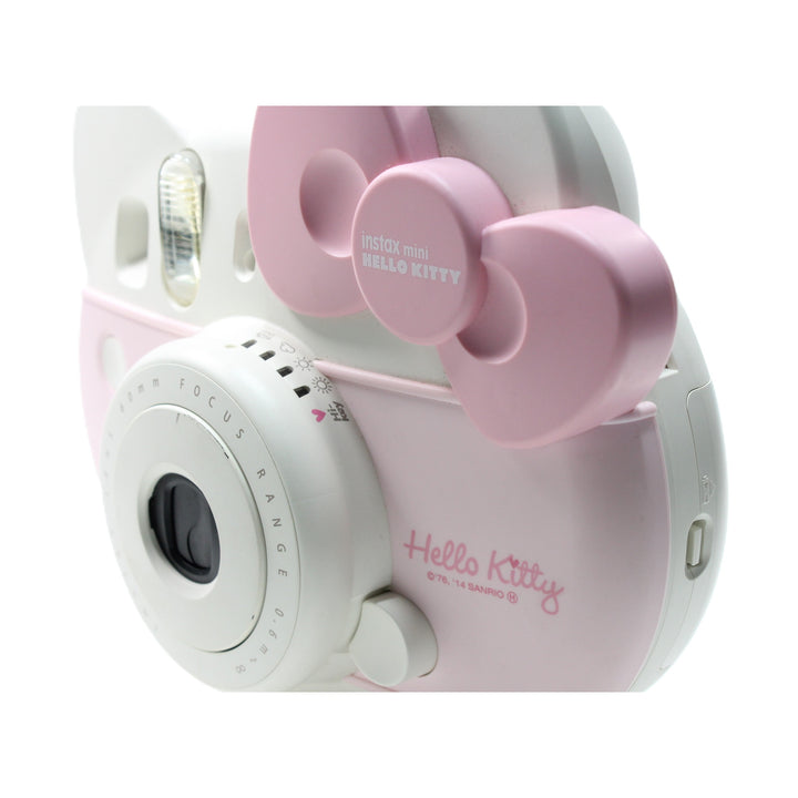 Close-up side profile of Fujifilm Instax mini HELLO KITTY camera highlighting textured pink bow and engraved lens details at ClubCamera.com