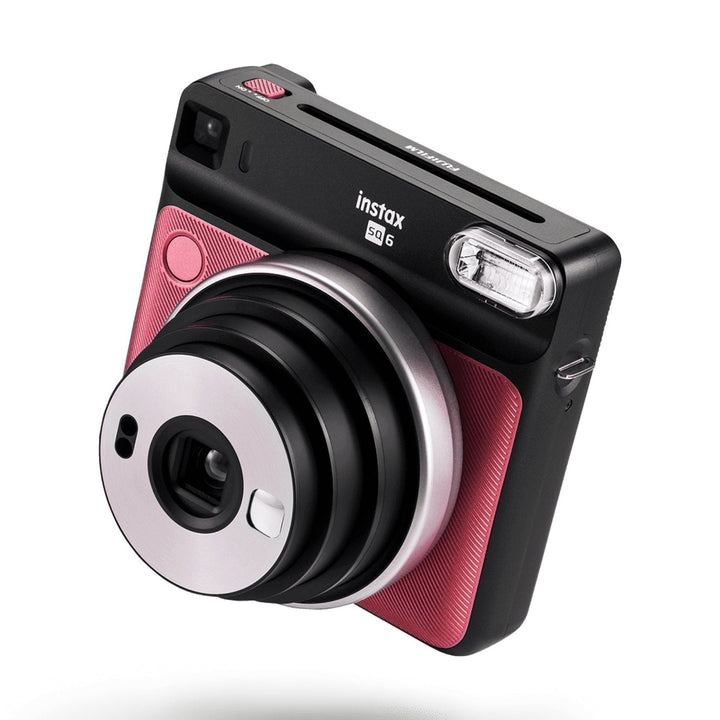 Side view of Ruby Red Fujifilm INSTAX Square SQ6 showing textured grip, USB-C port, and extended lens barrel from ClubCamera.com