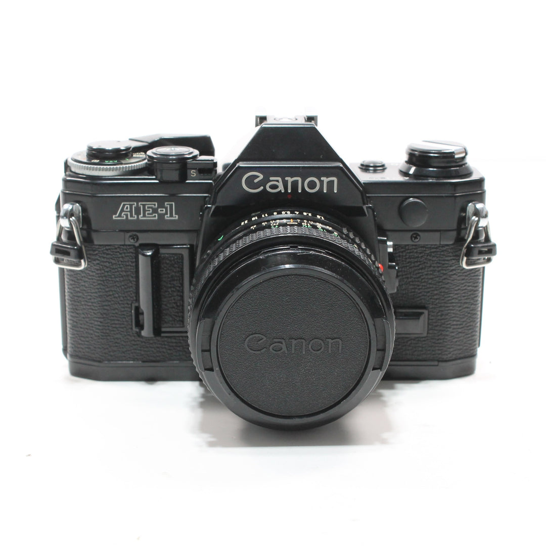 Canon AE-1 Black 35mm SLR film camera front view with lens cap on and silver logo details at ClubCamera.com