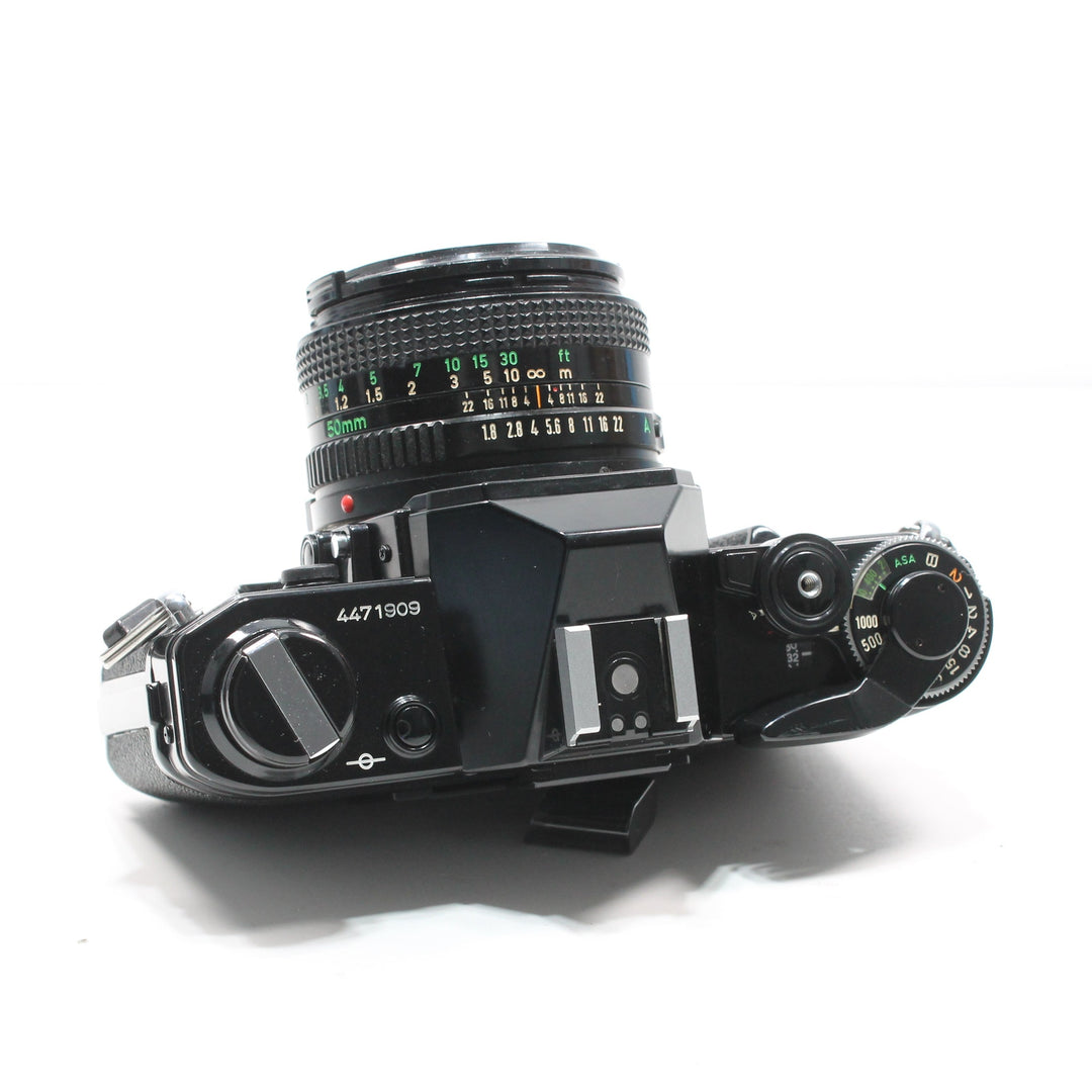Top-down Canon AE-1 Black 35mm camera with 50mm FD lens showing ASA mode dial and serial number at ClubCamera.com