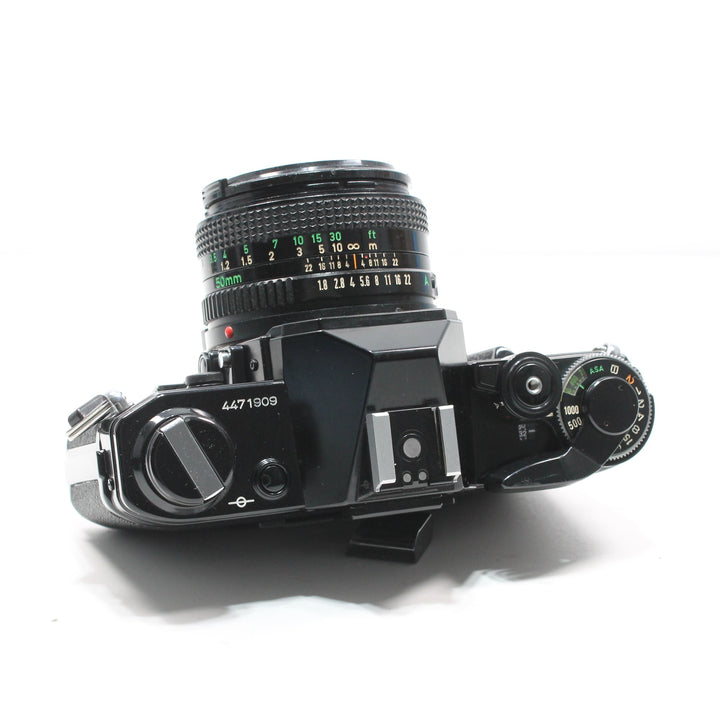 Top-down Canon AE-1 Black 35mm camera with 50mm FD lens showing ASA mode dial and serial number at ClubCamera.com