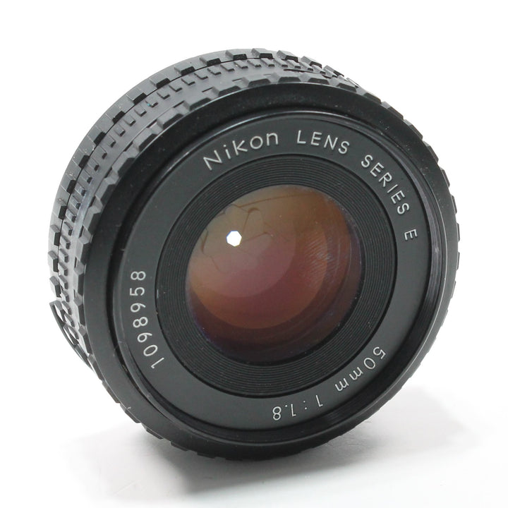 ClubCamera.com three-quarter view of Nikon Nikkor 50mm f/1.8 Series E lens with amber glass reflection and textured grip