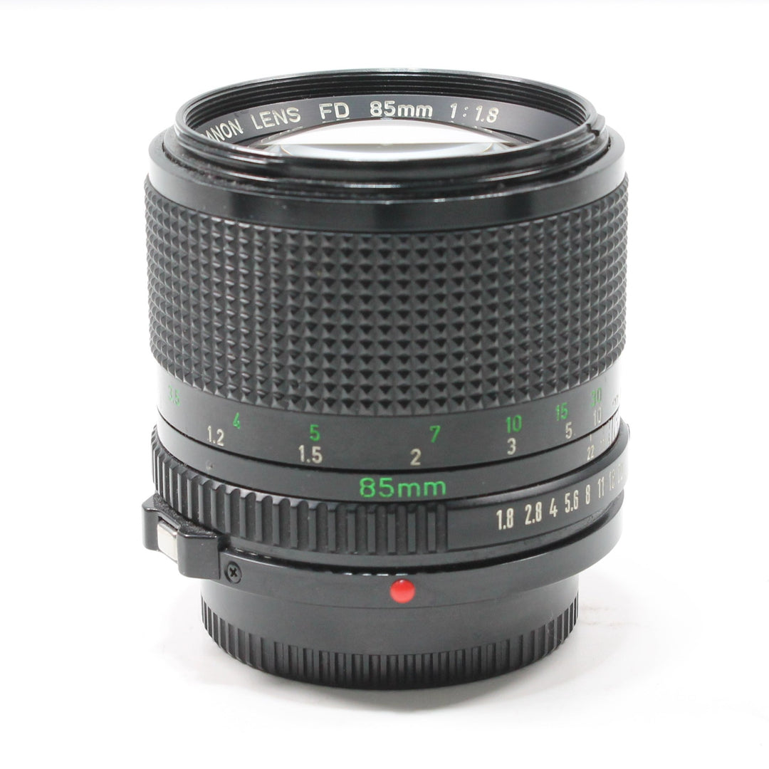 Close-up of black Canon FD 85mm f/1.8 prime lens with green engraved markings and red alignment dot from ClubCamera.com