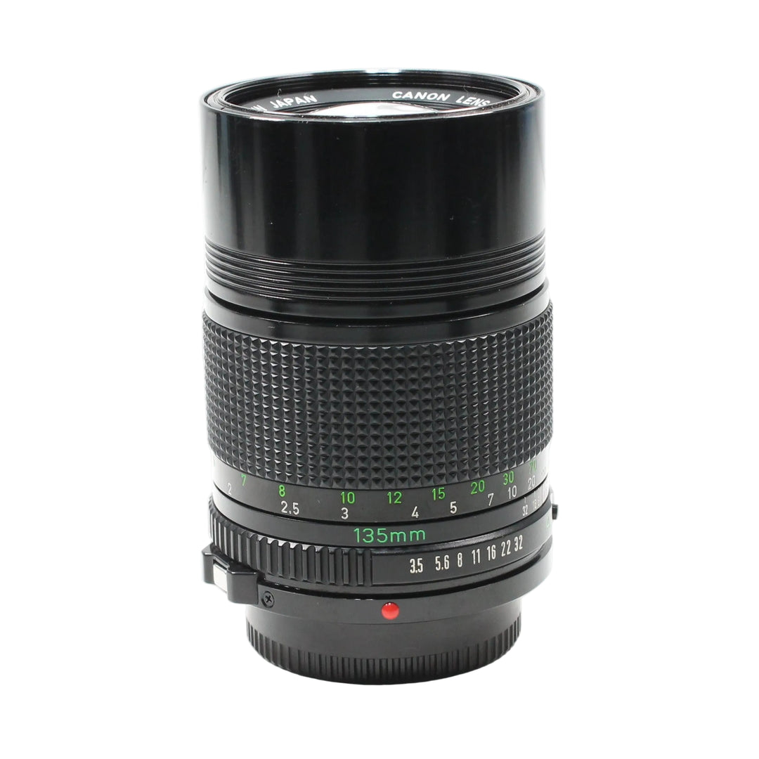 Canon FD 135mm f/3.5 manual focus telephoto lens by ClubCamera.com showing glossy black barrel with textured focus ring and green engraved markings