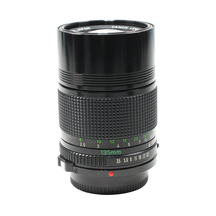 Canon FD 135mm f/3.5 manual focus telephoto lens by ClubCamera.com showing glossy black barrel with textured focus ring and green engraved markings