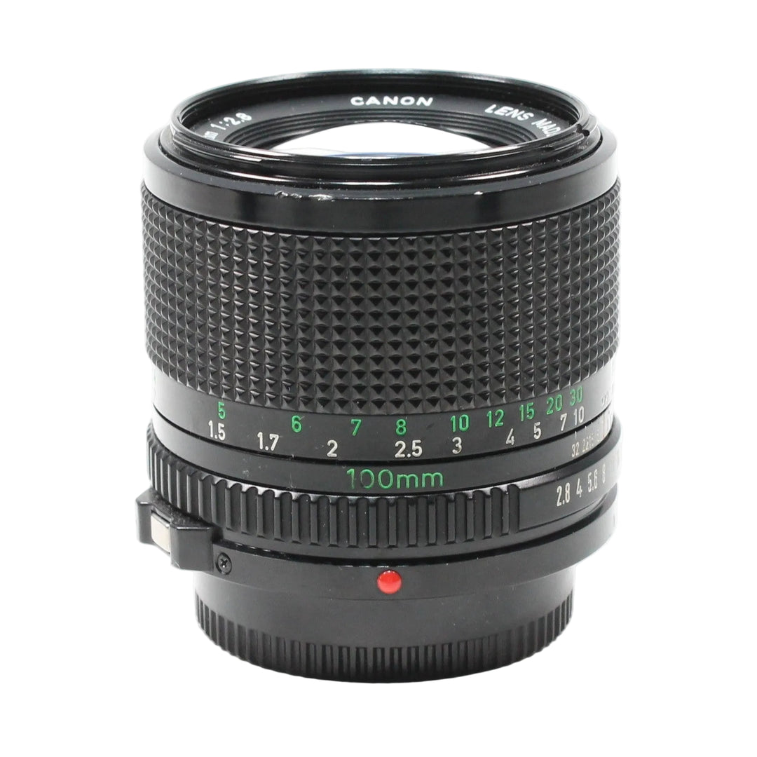 Close-up of Canon FD 100mm f/2.8 prime lens at ClubCamera.com featuring bright green focal length markings and ribbed focus collar