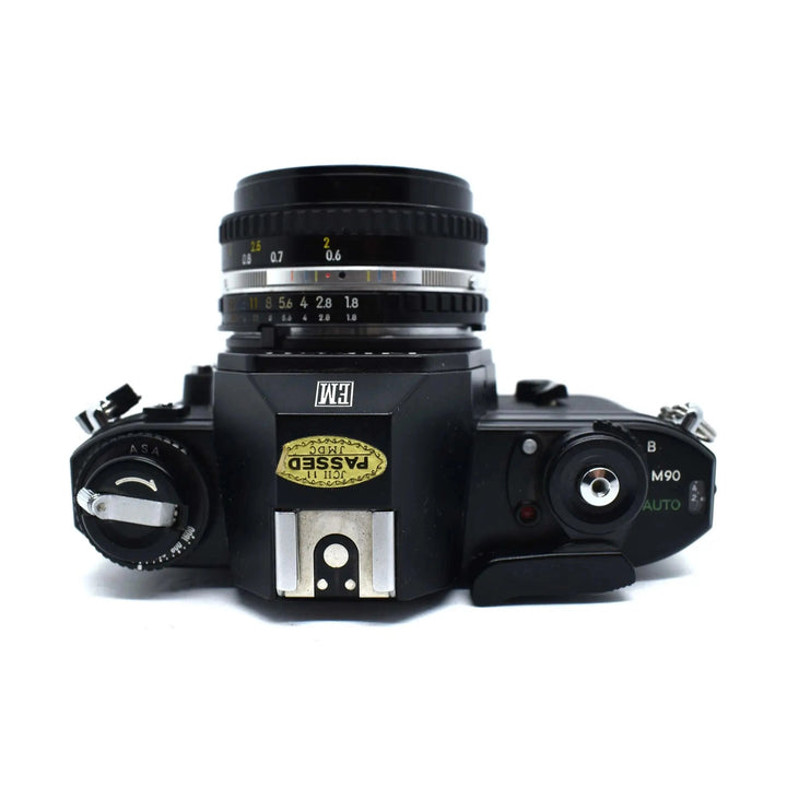 Top-down black Nikon EM 35mm SLR film camera showing aperture ring and ISO dial at ClubCamera.com