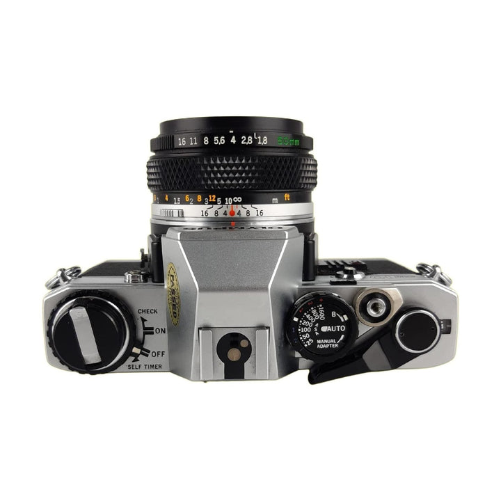 ClubCamera Olympus OM-10 aperture dial close-up showing green f-stops, AUTO mode, and distance scale on silver body