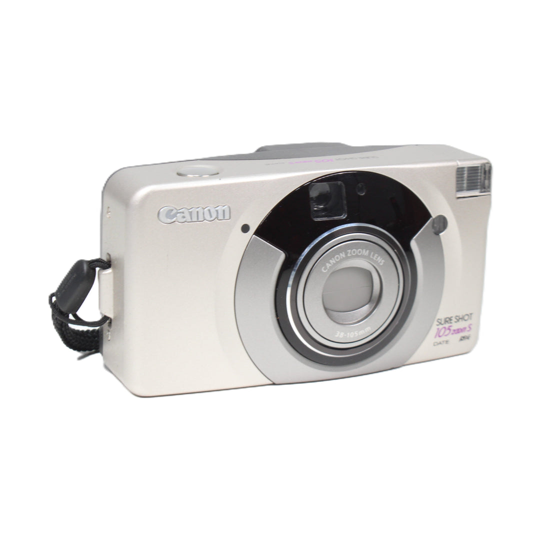 ClubCamera angled front shot of silver Canon Sure Shot 105 Zoom S with black wrist strap attached