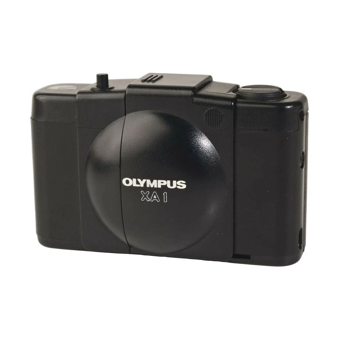 Side profile of compact black Olympus XA1 rangefinder film camera showing embossed logo and mode dial from ClubCamera.com