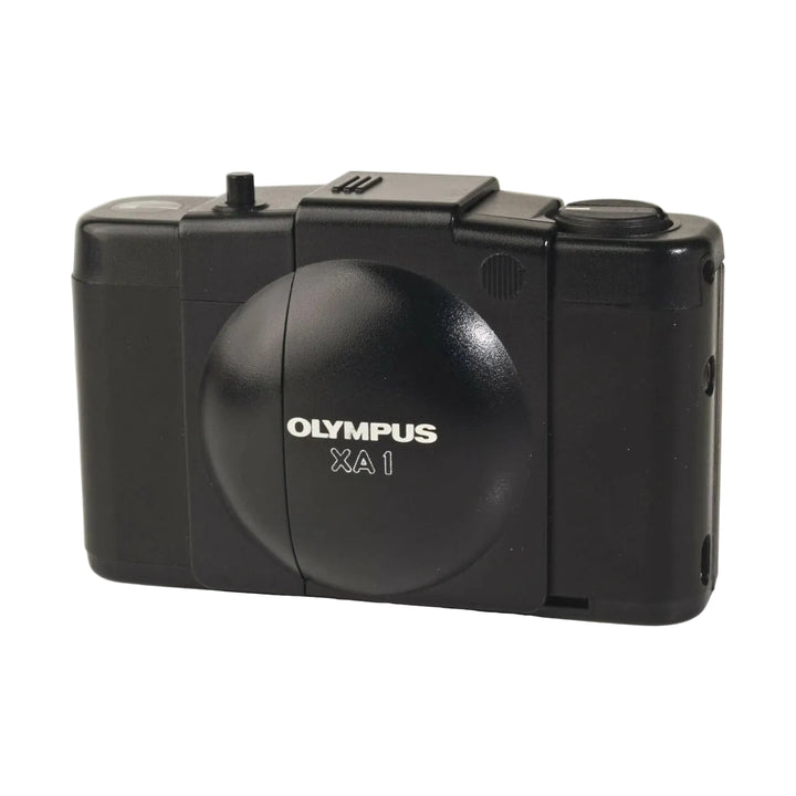 Side profile of compact black Olympus XA1 rangefinder film camera showing embossed logo and mode dial from ClubCamera.com