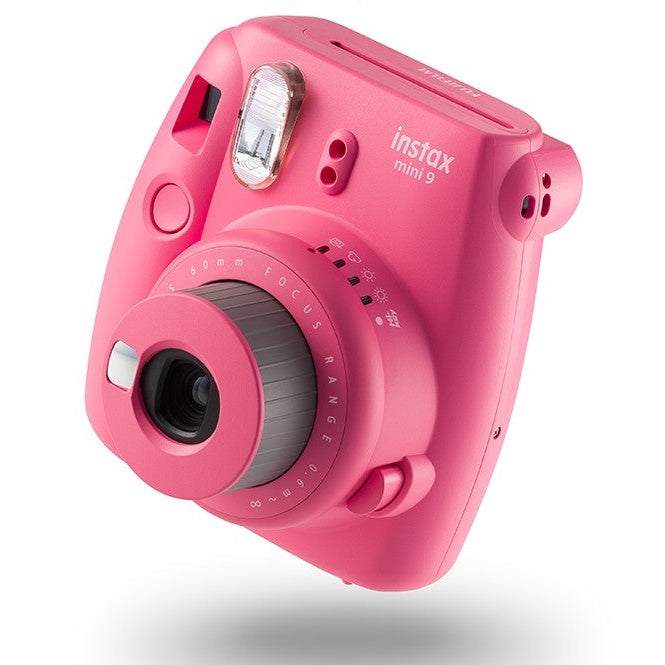 Fujifilm Instax Mini 9 Flamingo Pink instant camera by ClubCamera.com showing angled view of matte finish, silver flash, and focus ring