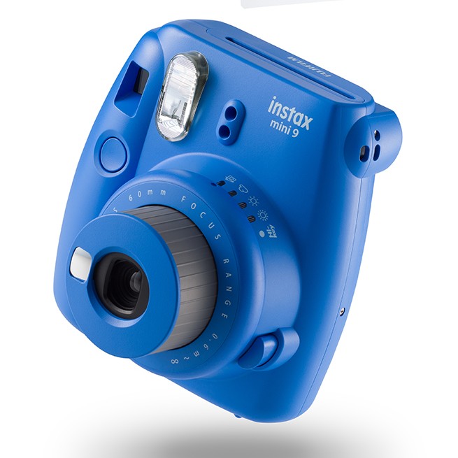 Side view of Fujifilm Instax Mini 9 cobalt blue showing textured focus ring, exposure icons, and compact portable design from ClubCamera.com