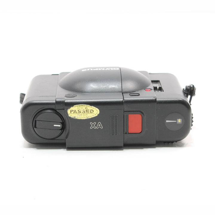 Side angle of black Olympus XA showing mode dial and inspection sticker at ClubCamera.com