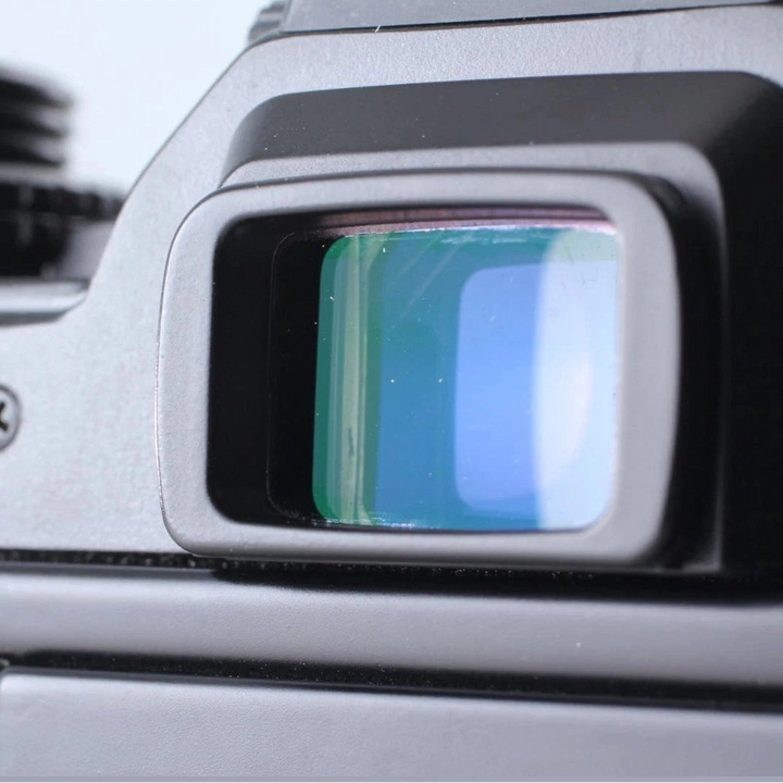 Close-up of green-blue tinted optical viewfinder eyepiece on black Olympus OM-4 SLR camera at ClubCamera.com